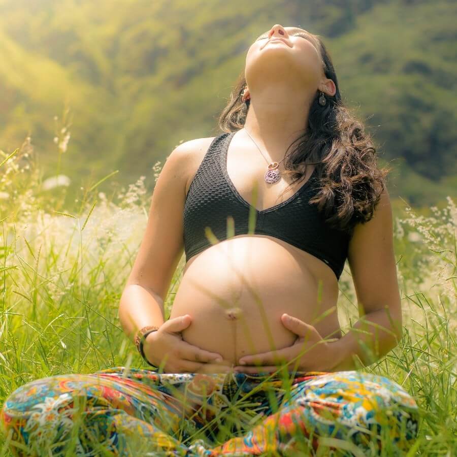 A woman sitting in a field holding her pregnant belly and taking in the sunlight.